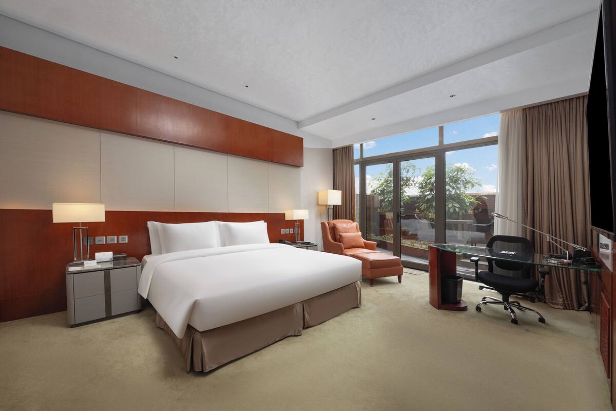 A hotel room with a large bed, a desk, a chair, and a view of the outdoors.