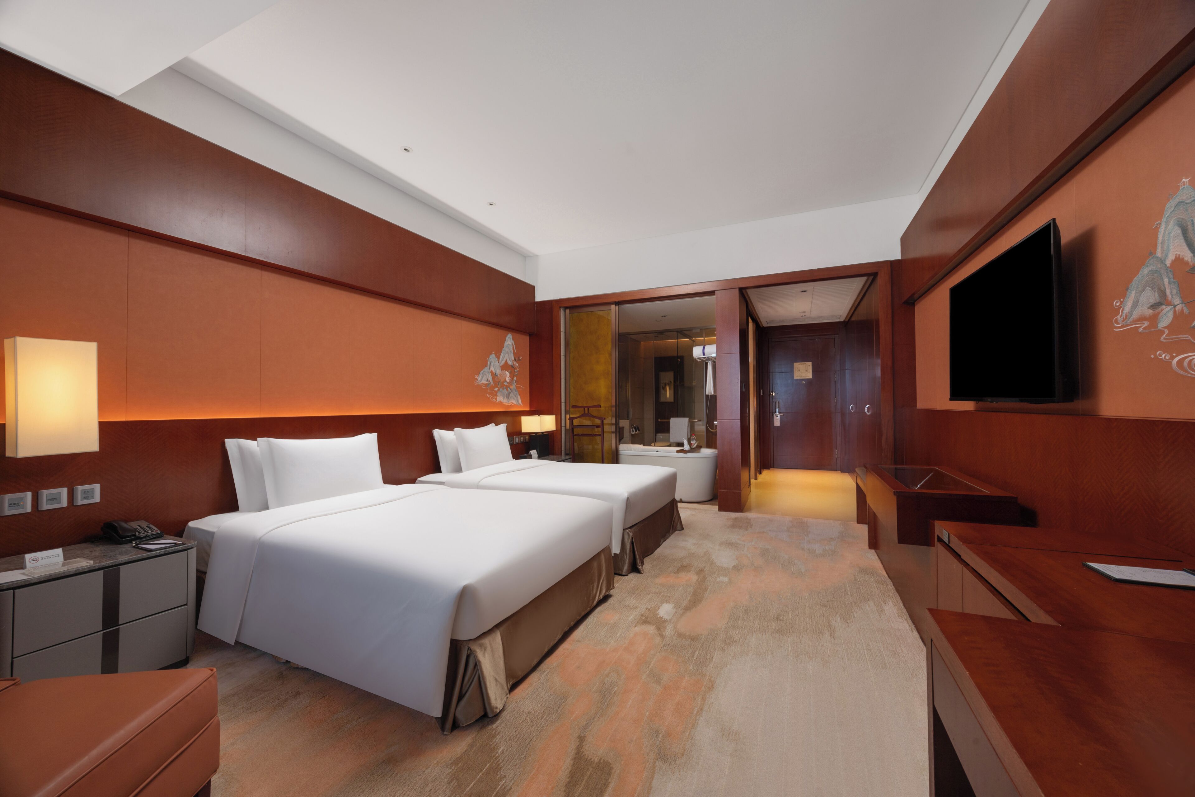A hotel room with two beds, a desk, a TV, and a bathroom visible through an open door.