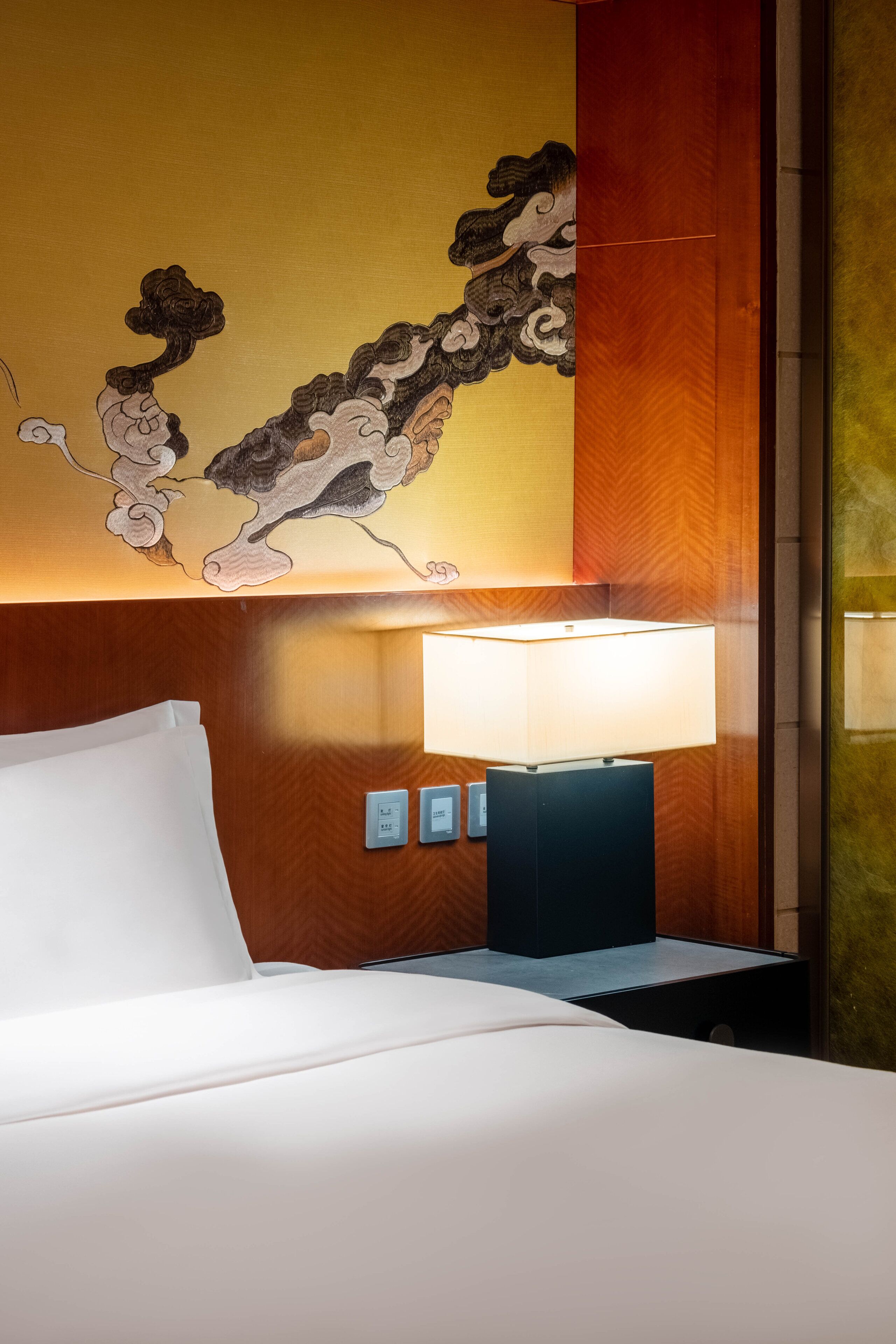 A hotel room with a bed, a wall-mounted lamp, and a decorative painting.