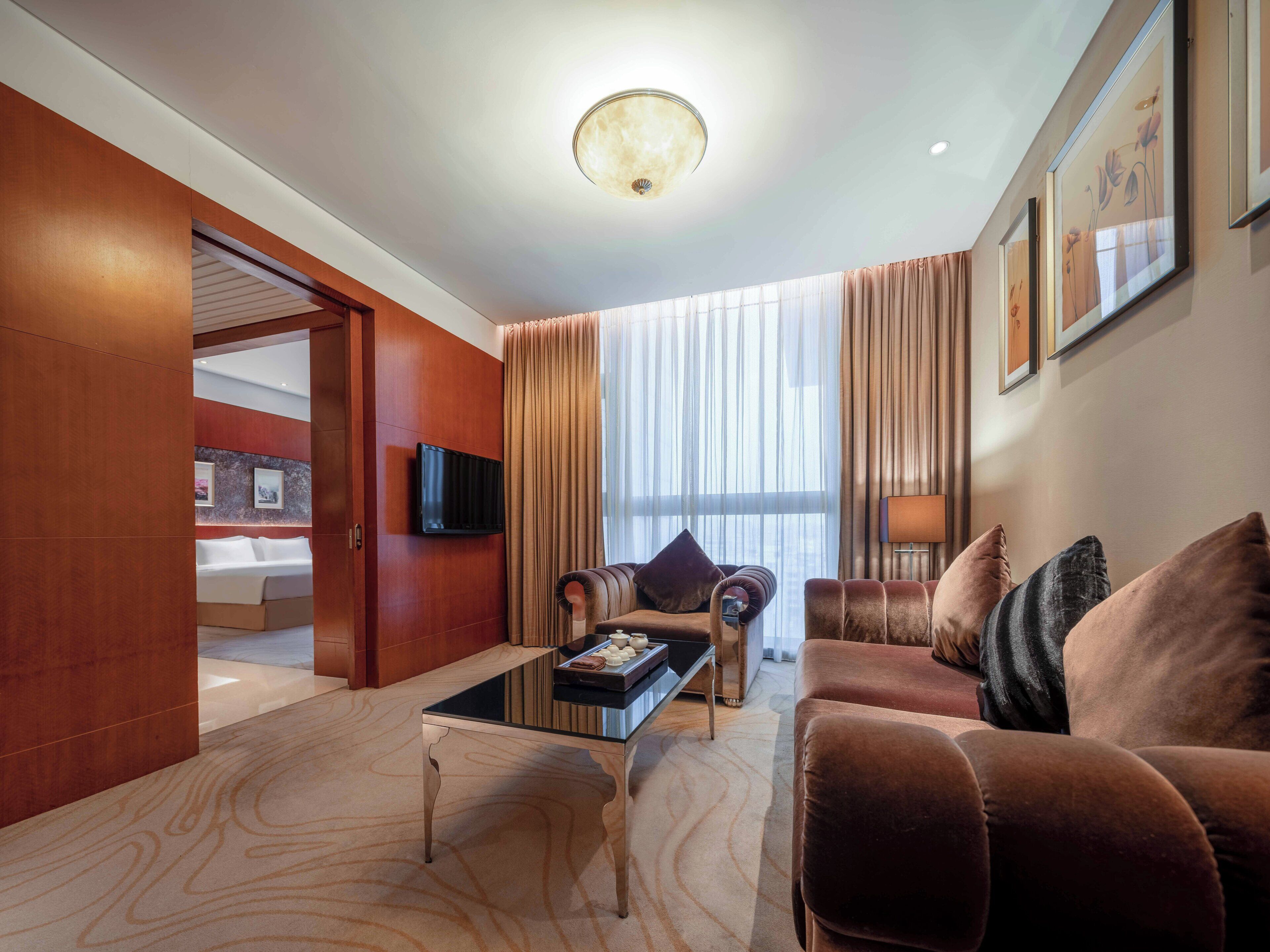 A modern hotel room with a large bed, a sofa, a coffee table, and a TV mounted on the wall.