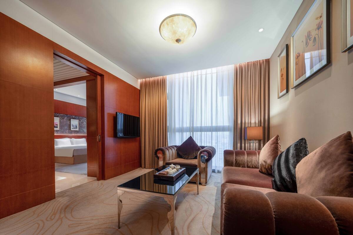 A modern hotel room with a large bed, a sofa, a coffee table, and a TV mounted on the wall.