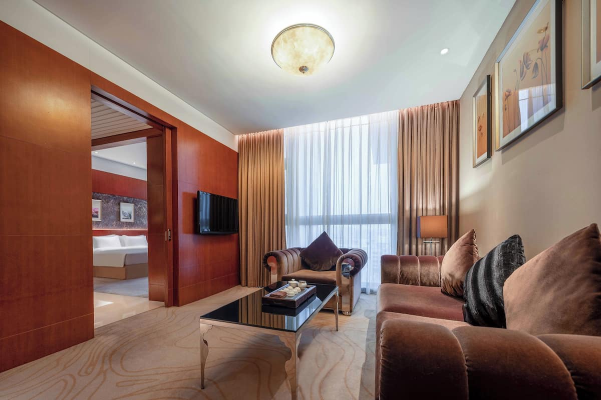 A modern hotel room with a large bed, a sofa, a coffee table, and a TV mounted on the wall.