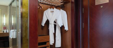 A wooden walk-in closet with two white robes hanging on a rack, a wooden shelf with shoes, and a door with a plaque.