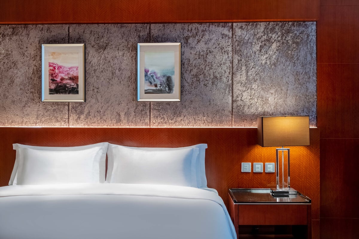 A hotel room with a large bed, a nightstand with a lamp, and two framed pictures on the wall.