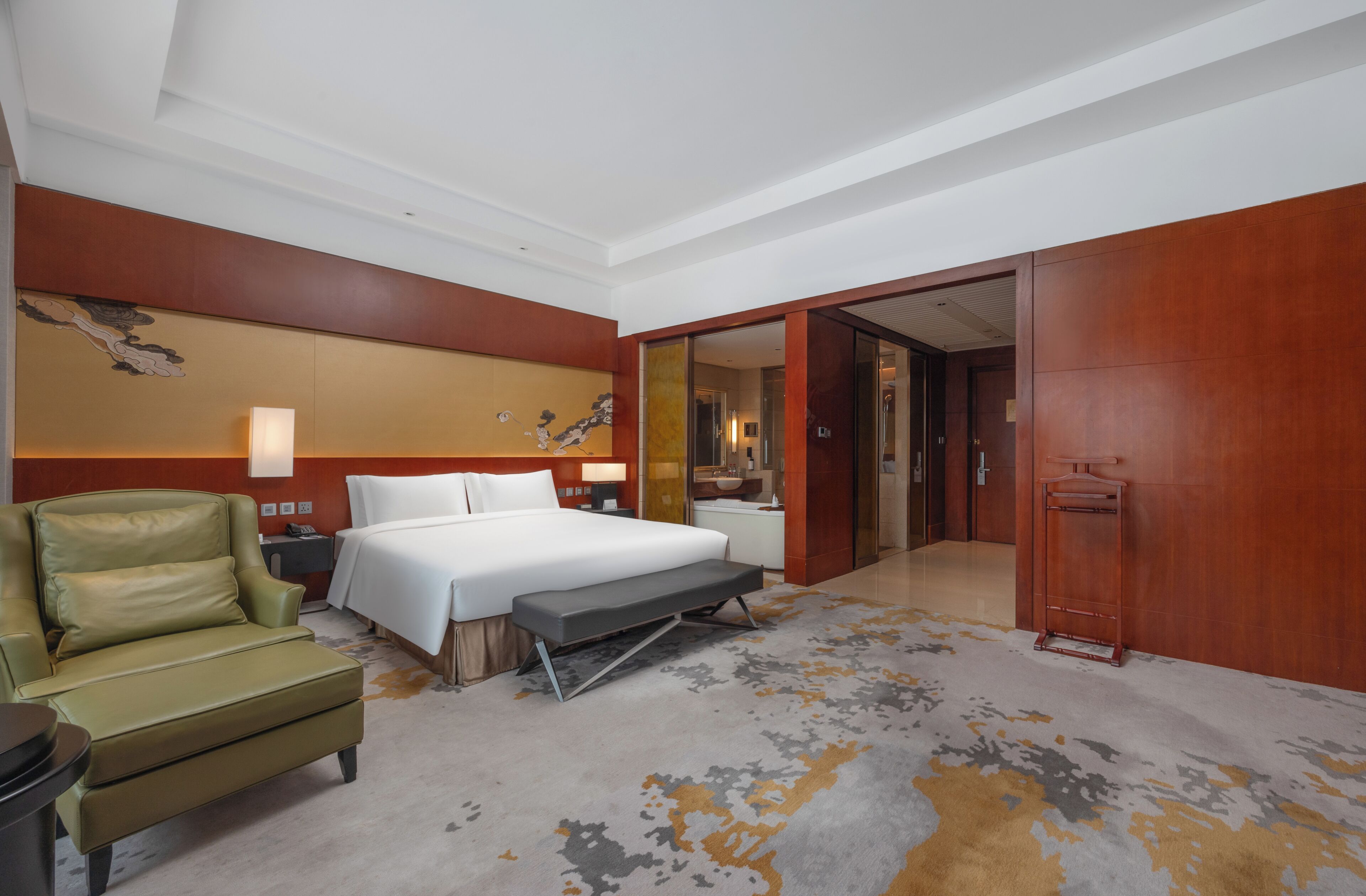 A hotel room with a bed, a chair, a desk, a bathroom, and a door.