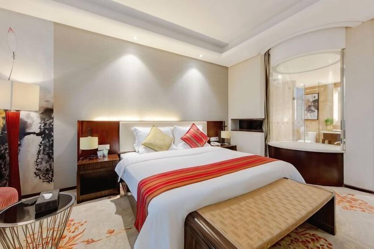 A hotel room with a large bed, bedside tables, a mirror, and a small seating area.