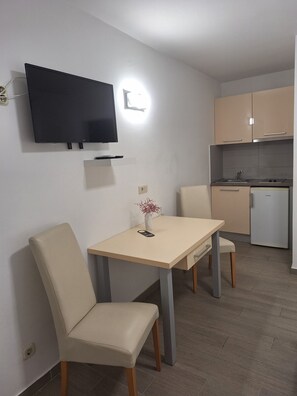 Una pequeña kitchenette con refrigerador, estufa y pileta. Hay una mesa de comedor con dos sillas y un televisor de pantalla plana montado en la pared.