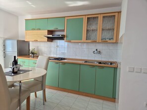 Una cocina moderna con gabinetes verdes, una encimera blanca, una mesa de comedor con sillas y una estufa empotrada.