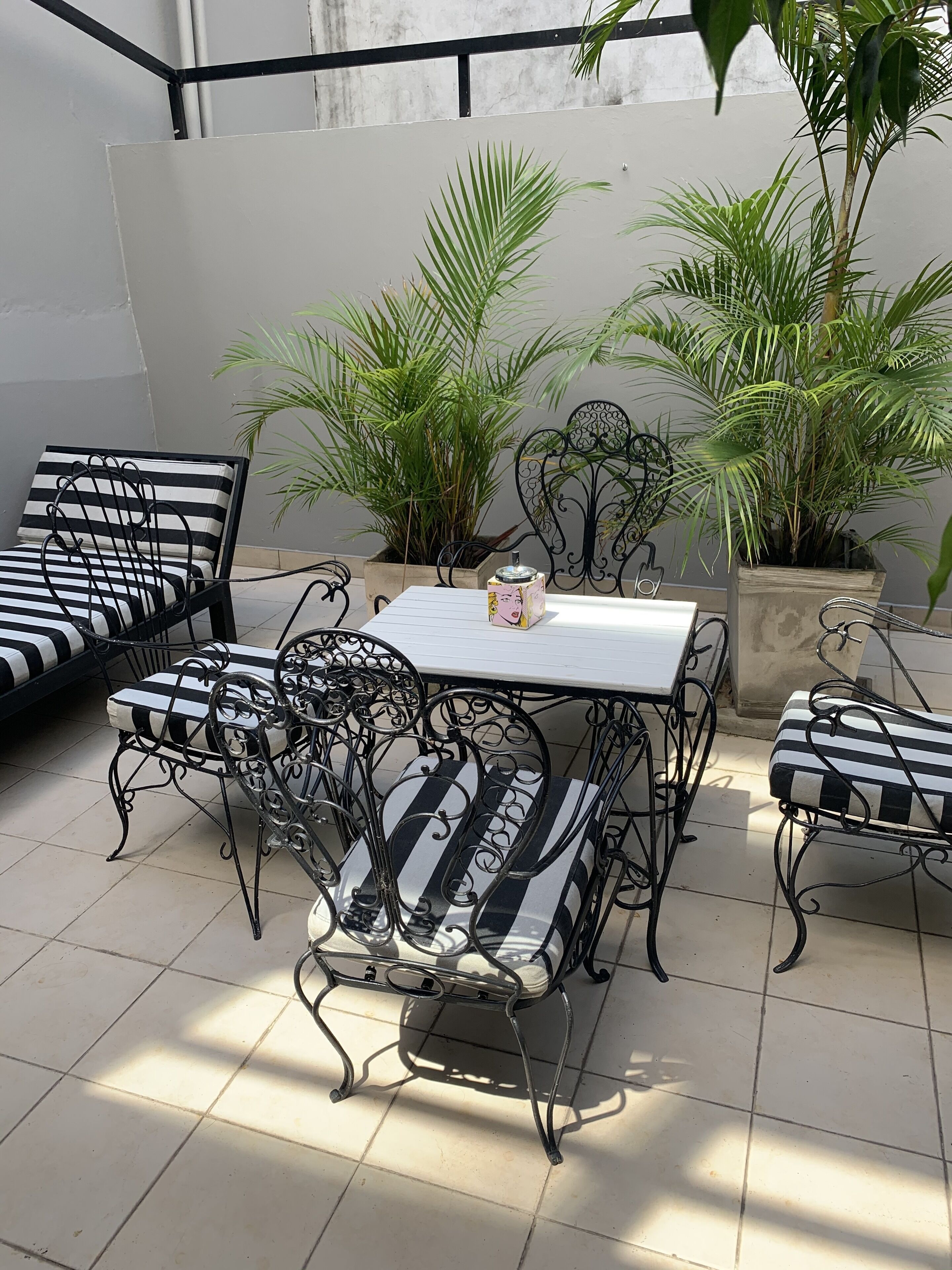 A patio area with a table and four striped lounge chairs, surrounded by potted plants.