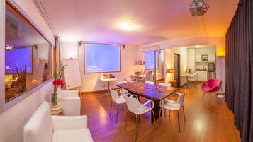 Una sala de estar moderna con comedor, cocina y una pantalla de proyector.