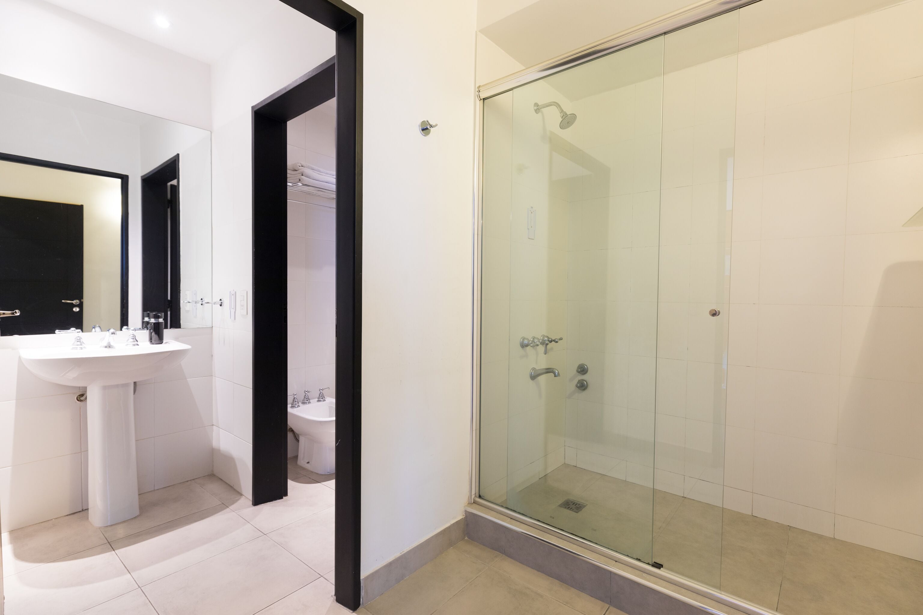 Un baño moderno con ducha envuelta en vidrio, un lavamanos blanco y un inodoro.