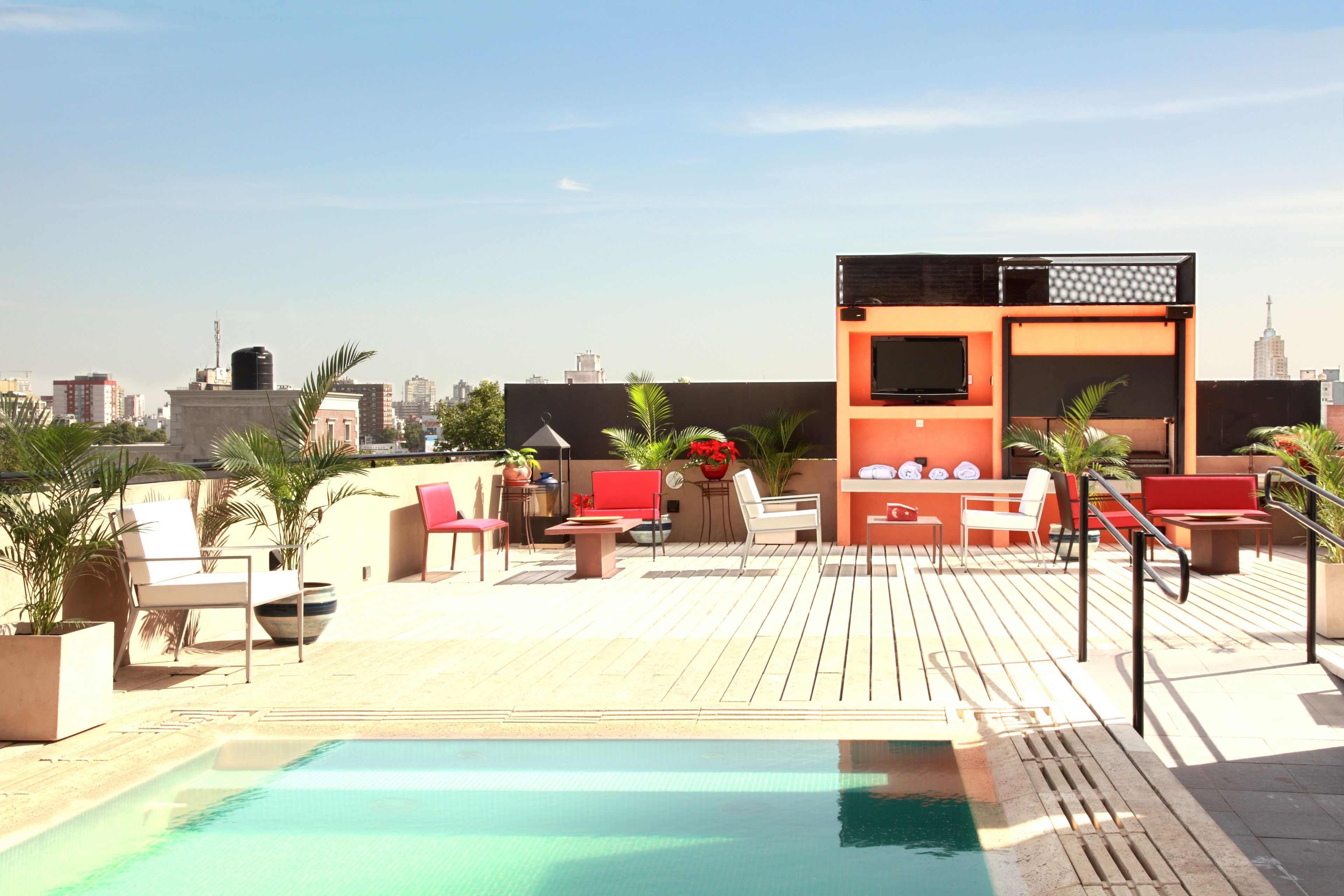 A rooftop pool area with lounge chairs, a barbecue area, and city views.