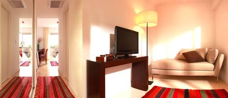 Una sala de estar moderna con un televisor de pantalla plana sobre un mueble de madera, un sofá color beige y una alfombra a rayas rojas.
