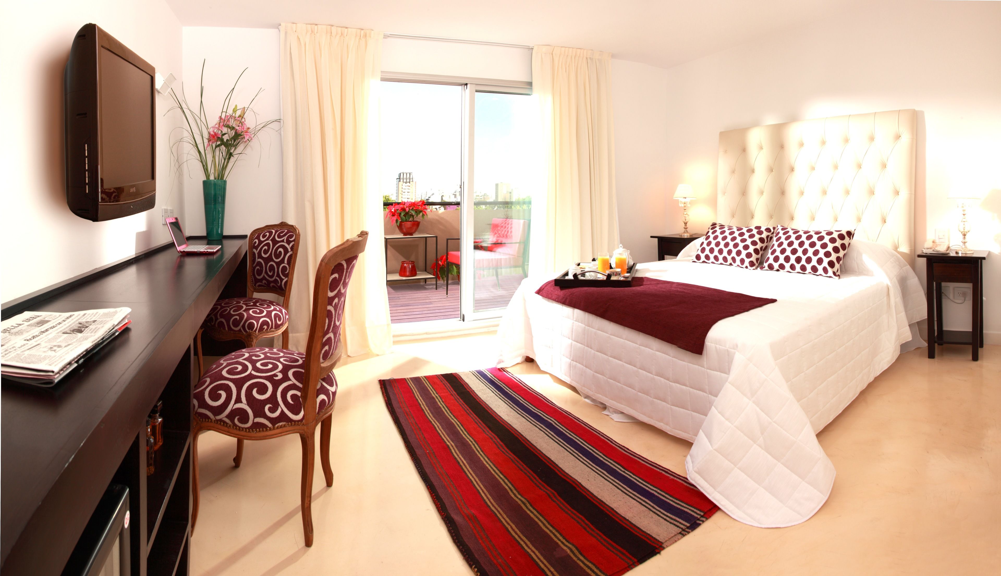 A hotel room with a bed, a desk with a laptop, a chair, a TV, and a view of the outdoors.