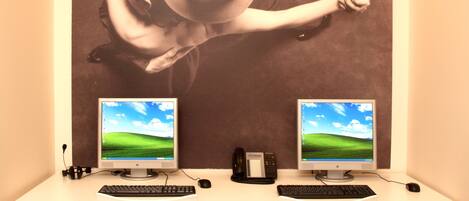 Un puesto de trabajo con dos monitores, una fotografía grande montada en la pared, dos sillas blancas y dos computadoras de escritorio.