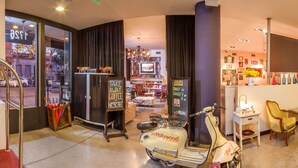 Un hall d’hôtel décoré avec un scooter vintage, un bar à café et un espace salon avec des fauteuils et une table.