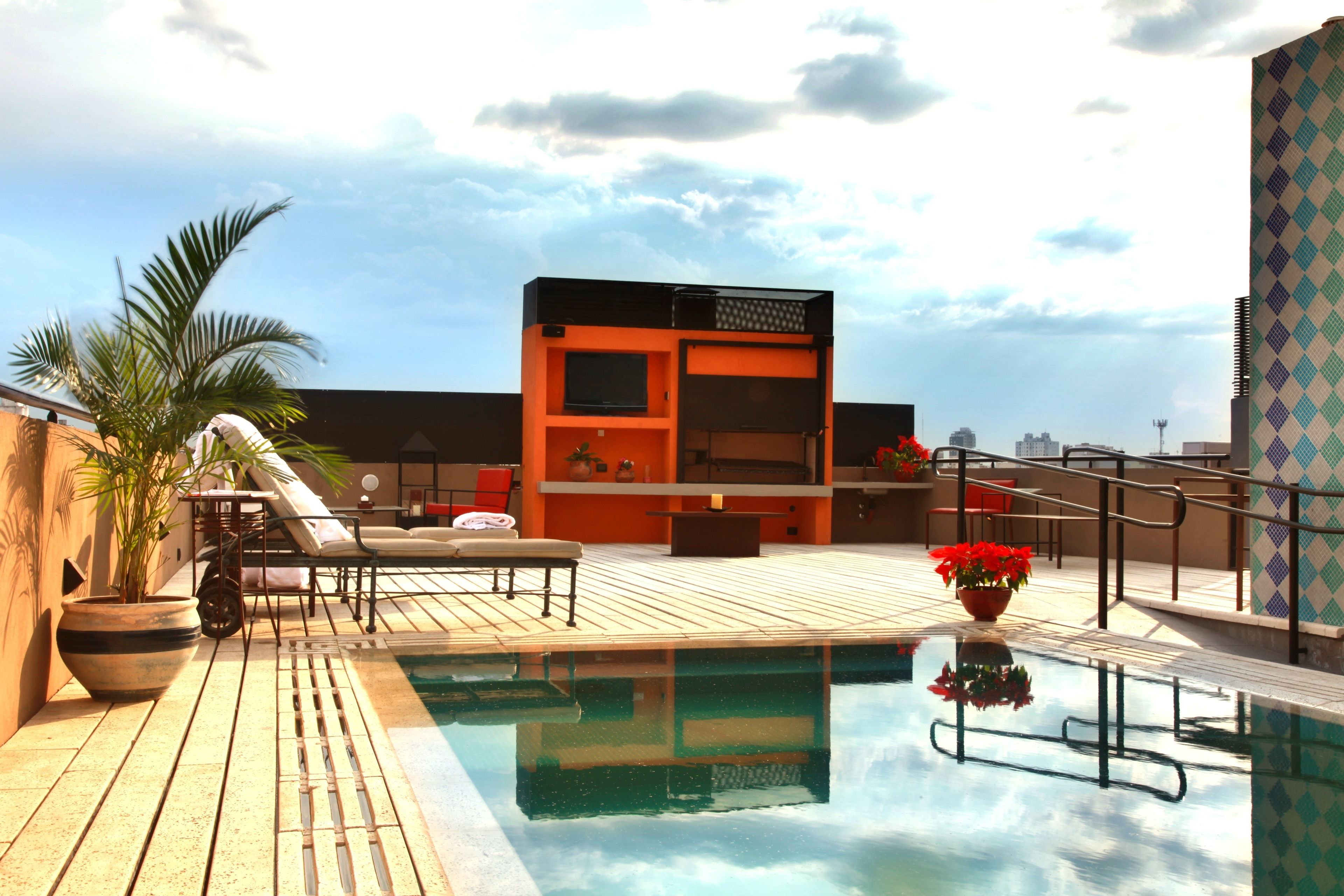 A rooftop pool area with lounge chairs, a small bar, and a potted plant.