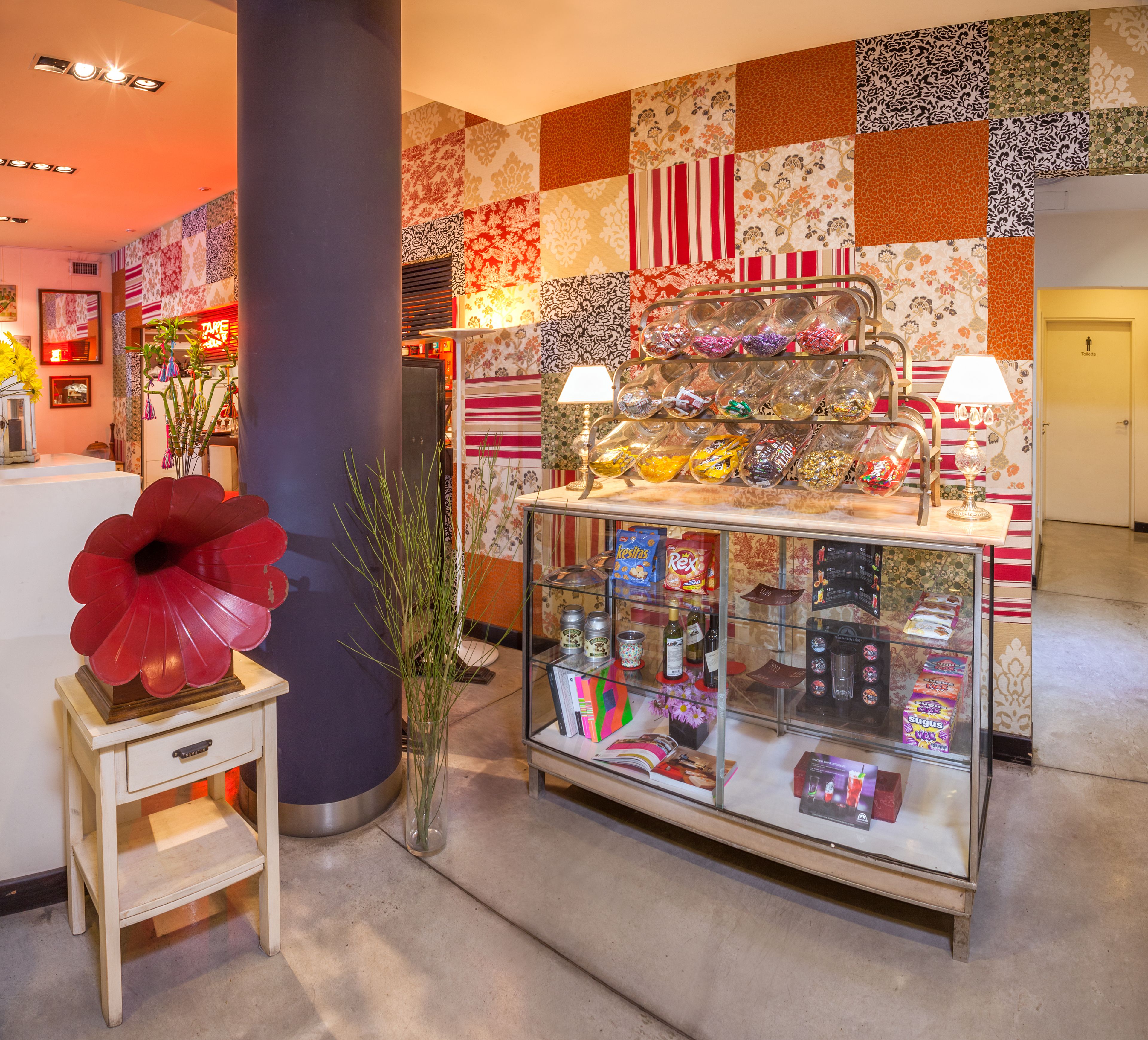 Un vestíbulo de hotel con una pared decorativa, una vitrina con aperitivos y una escultura floral roja.