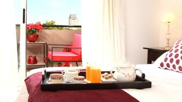 A hotel room with a bed, a tray with breakfast items, a red chair, and a view of the city.