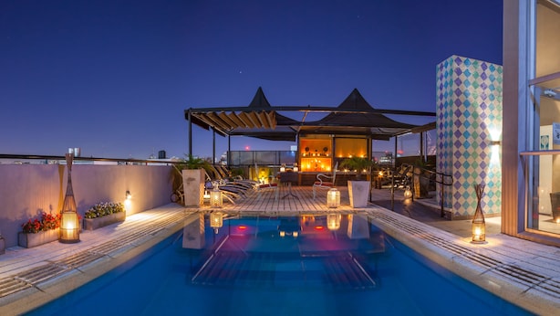 Un espace piscine sur le toit, doté d'une structure en verre, de chaises longues et d'un éclairage d'ambiance.