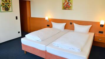 Cama doble con ropa de cama blanca, dos mesitas de noche con lámparas y dos cuadros en las paredes.