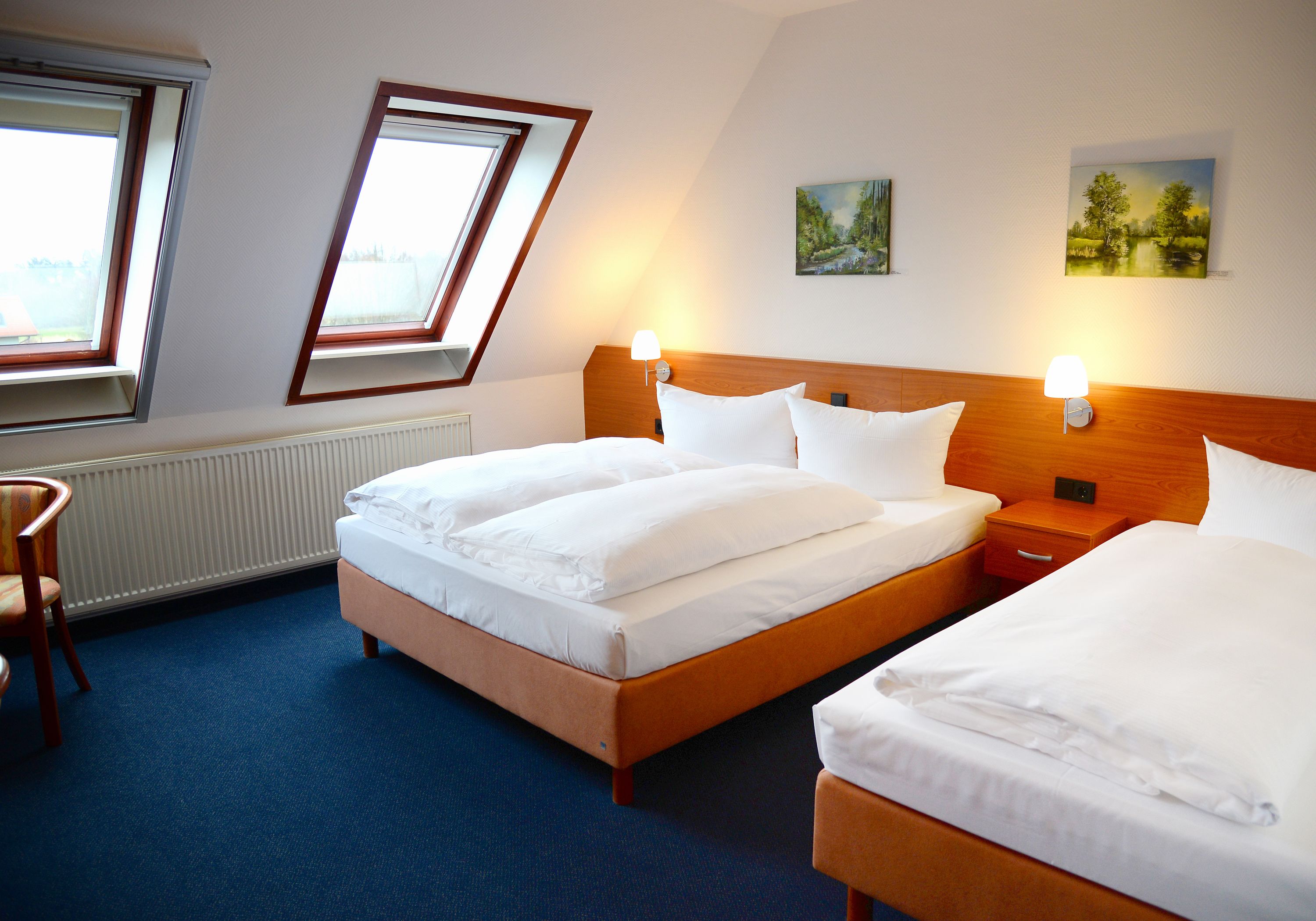A hotel room with two beds, a wooden headboard, a chair, and a painting on the wall.