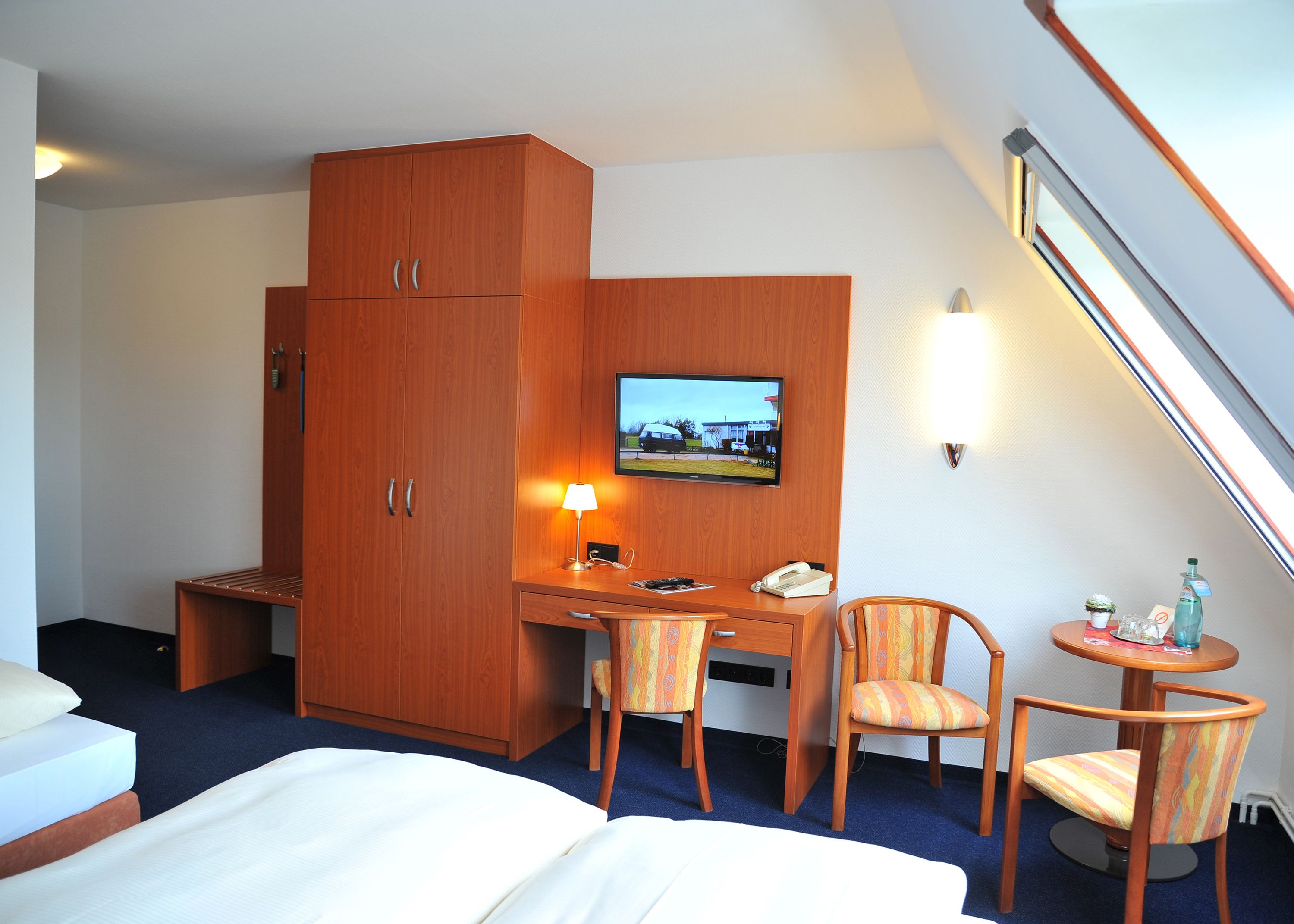 A hotel room with a bed, a desk with a chair, a television, a lamp, and a small table with a chair.