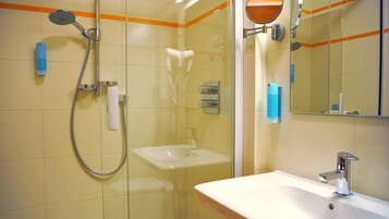 Un baño con cabina de ducha de vidrio, un lavamanos blanco y un espejo con una franja naranja.