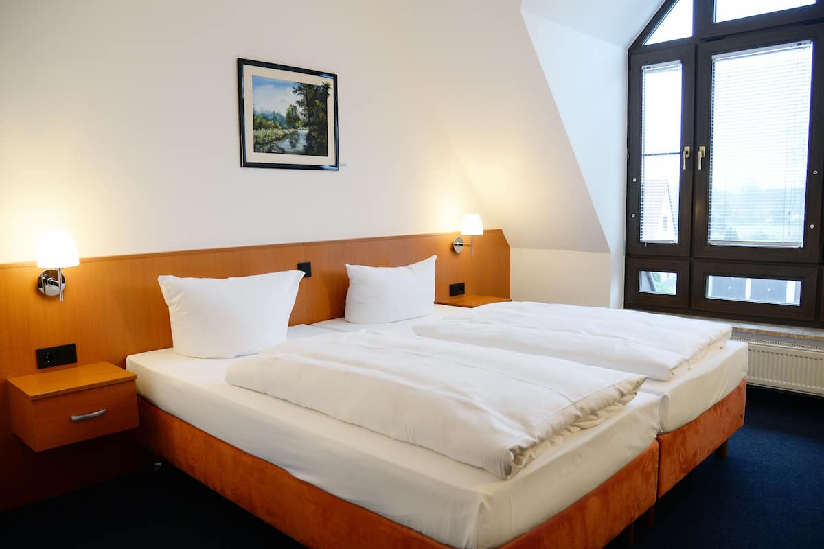 A double bed with white linens, wooden headboard, bedside tables with lamps, and a framed picture on the wall.