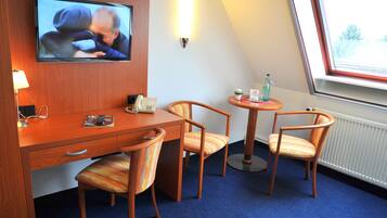Ein Hotelzimmer mit einem Holztisch, zwei Stühlen, einem Fernseher, einem kleinen Tisch mit einer Lampe, einer Topfpflanze und einem Fenster mit Blick.