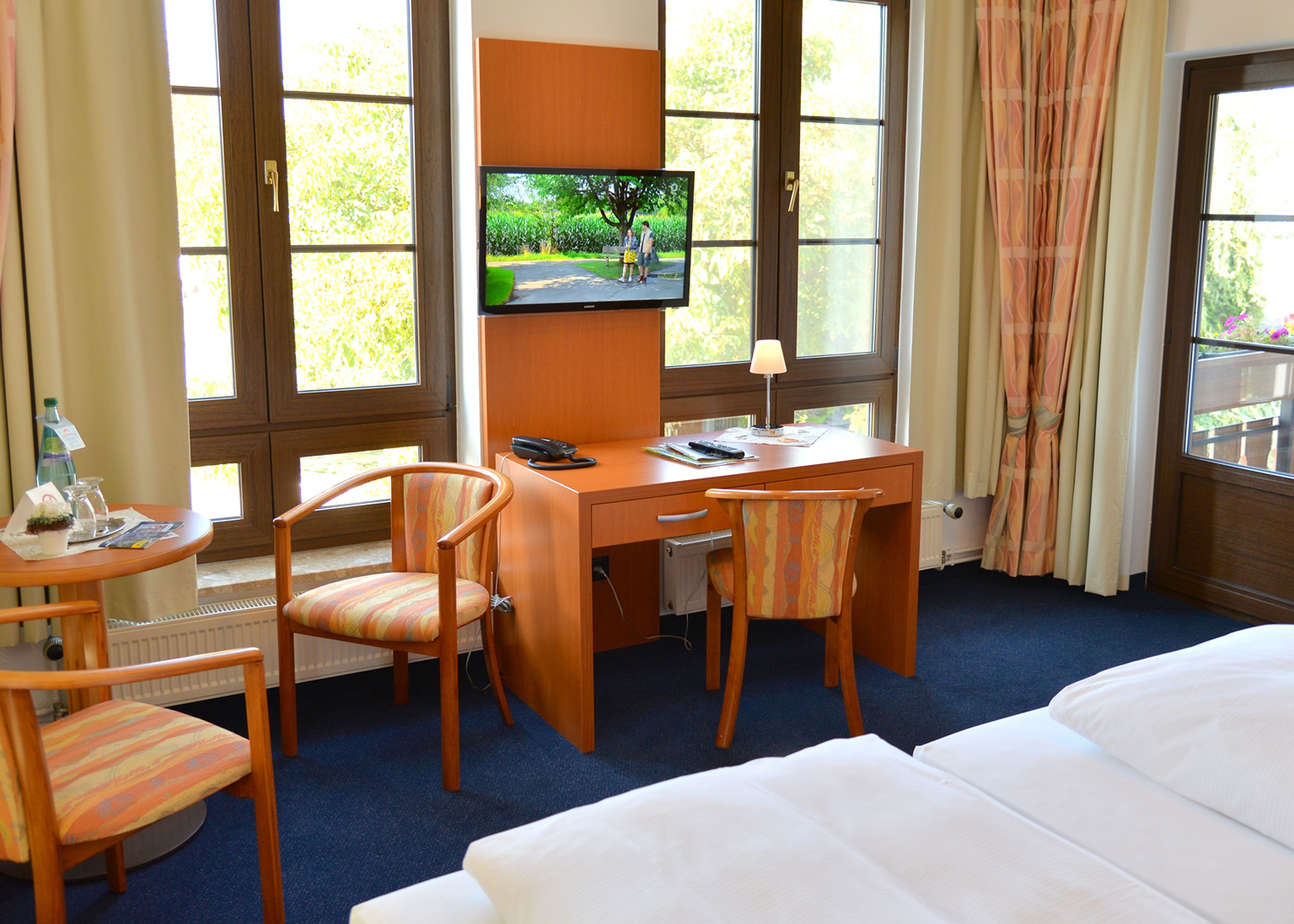 A hotel room with a wooden desk, two chairs, a television, and a bed.