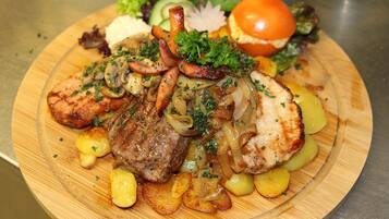 A wooden plate with grilled meat, potatoes, and vegetables.