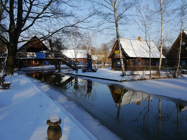 A winter scene with a snow-covered canal, wooden buildings, and a bridge.