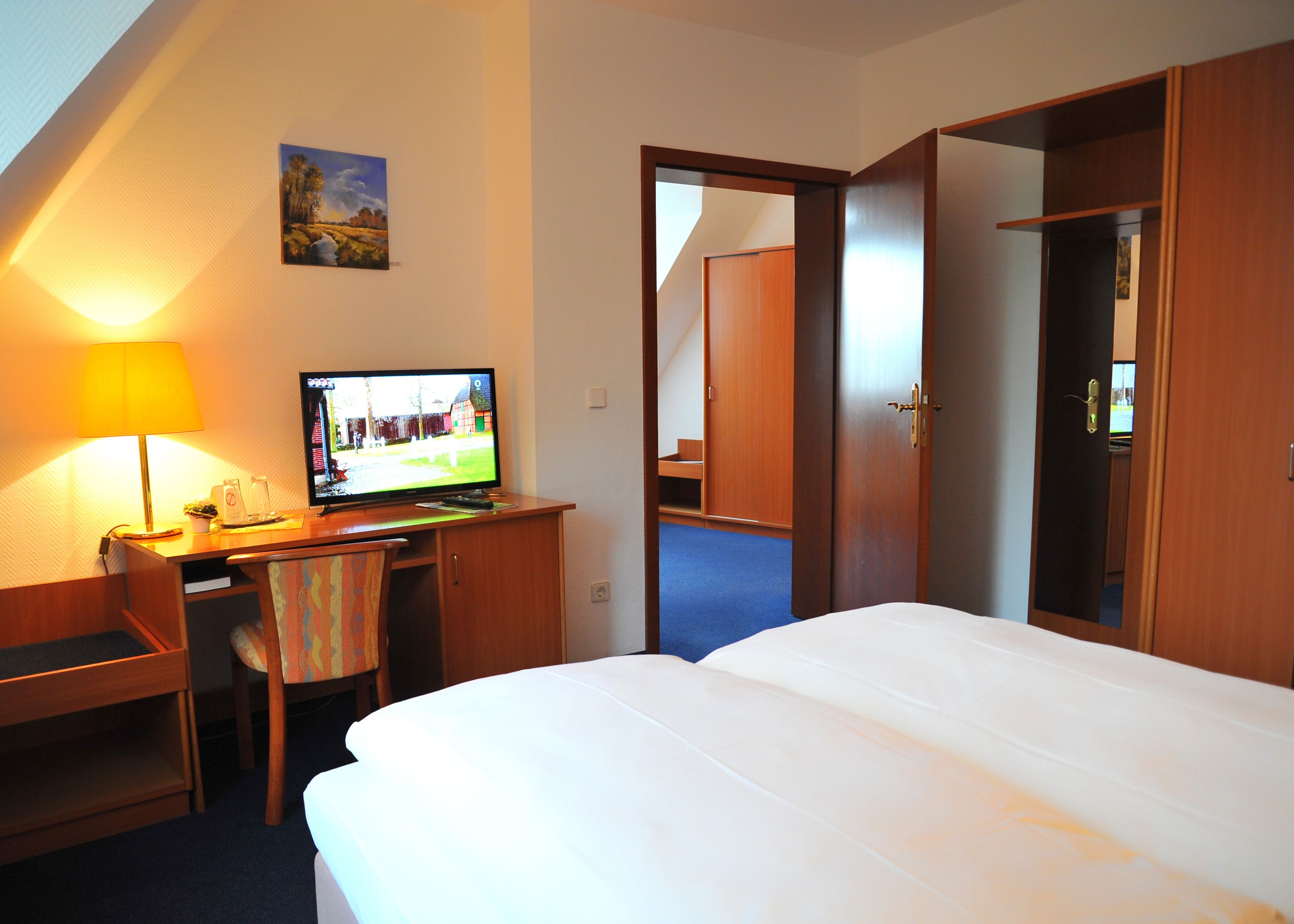 A hotel room with a bed, desk, chair, TV, and wardrobe.