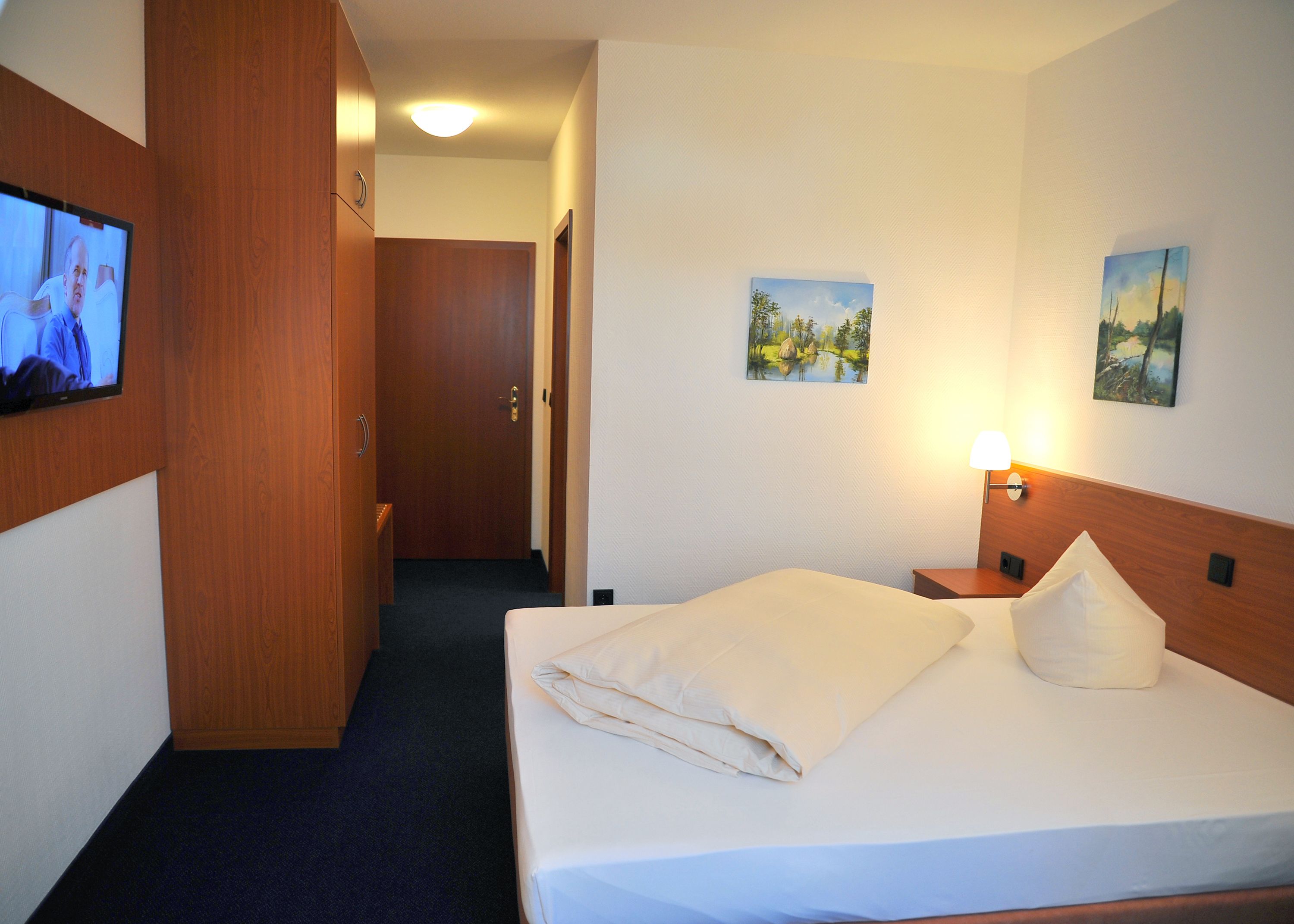 A hotel room with a bed, a TV on the wall, and two paintings.