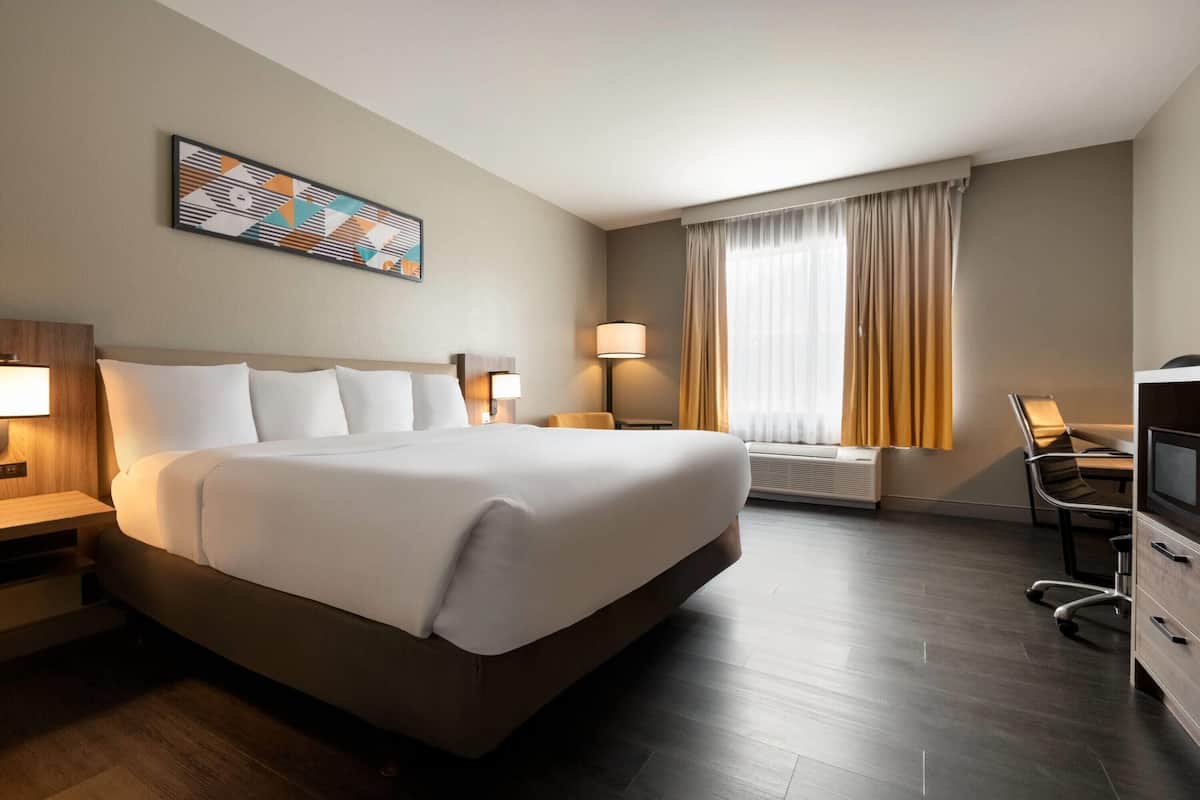 A hotel room with a large bed, bedside lamps, a desk with a chair, a TV, and a window with curtains.
