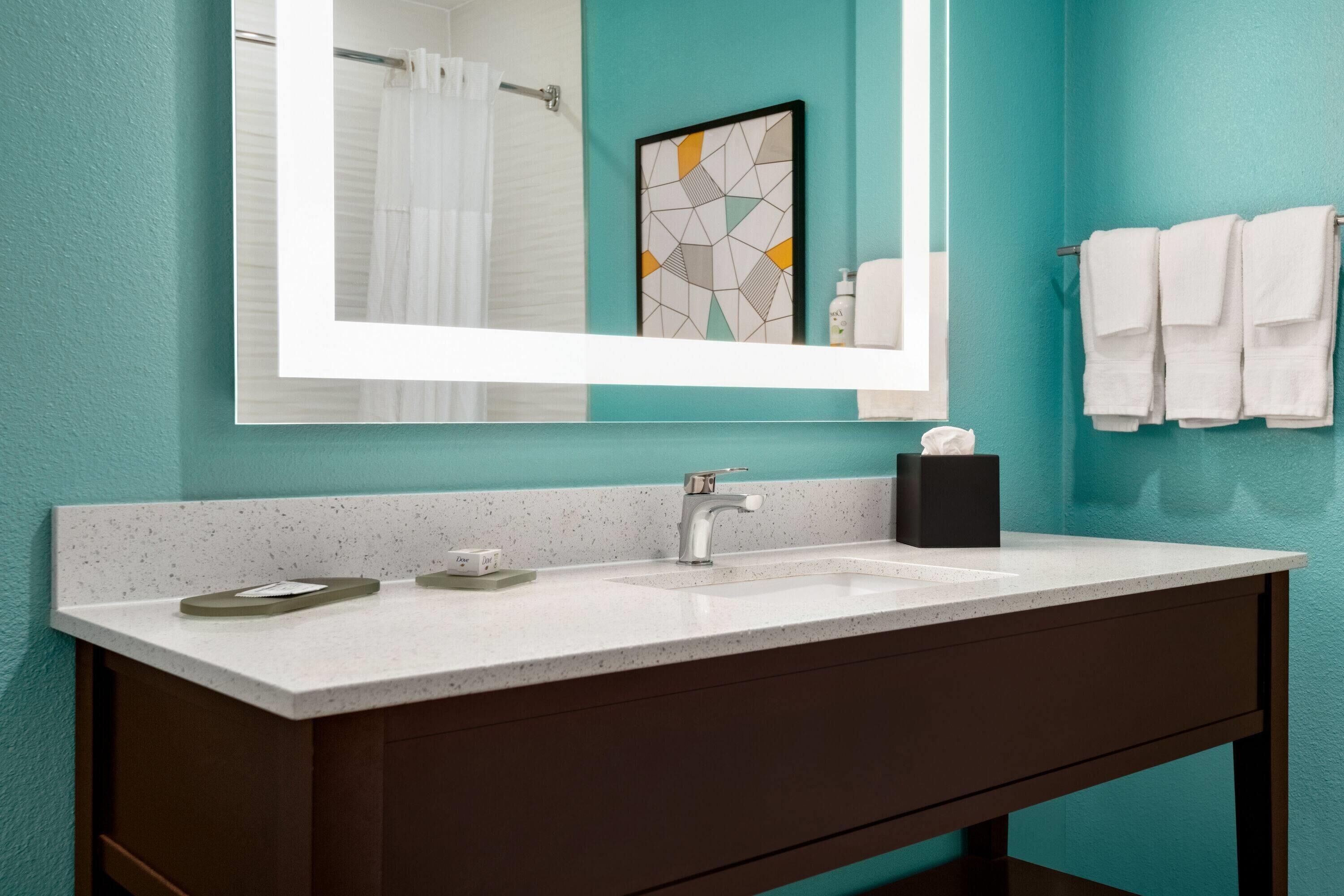 A bathroom with a large mirror, a sink, and a towel rack.