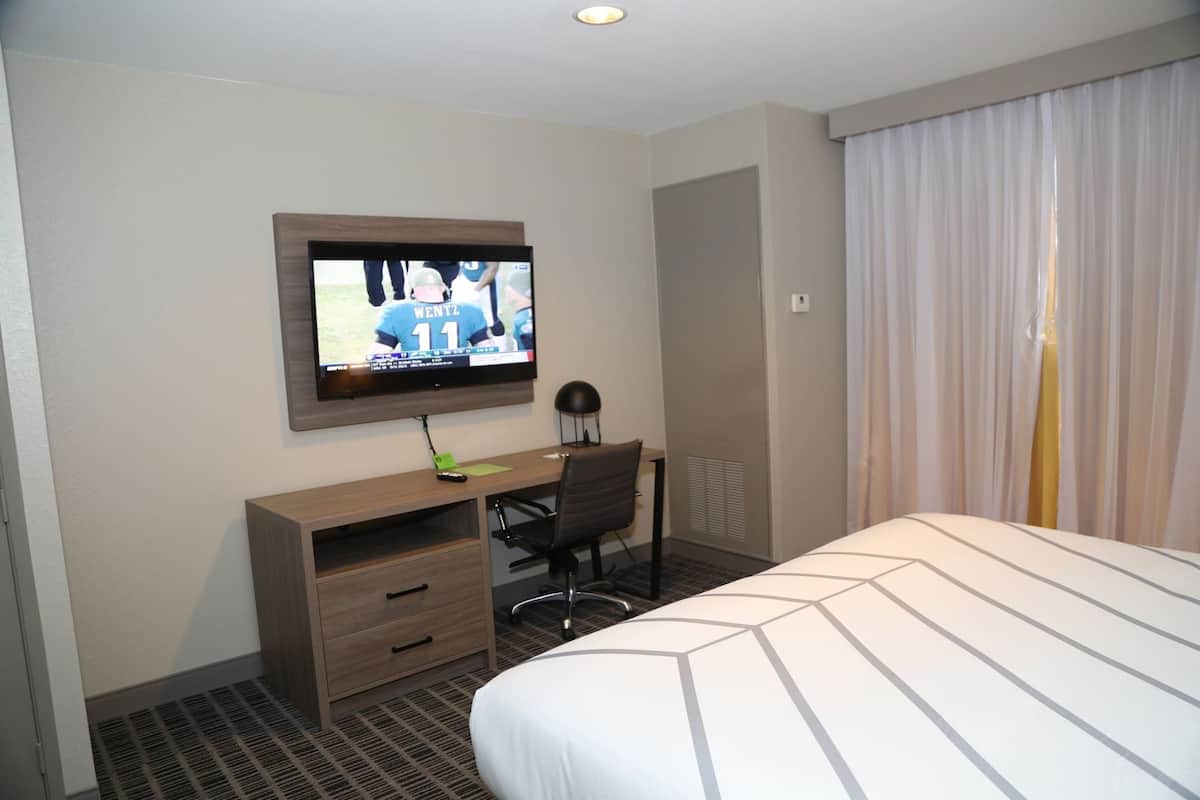 A hotel room with a bed, a desk with a computer, a television, and a window with curtains.