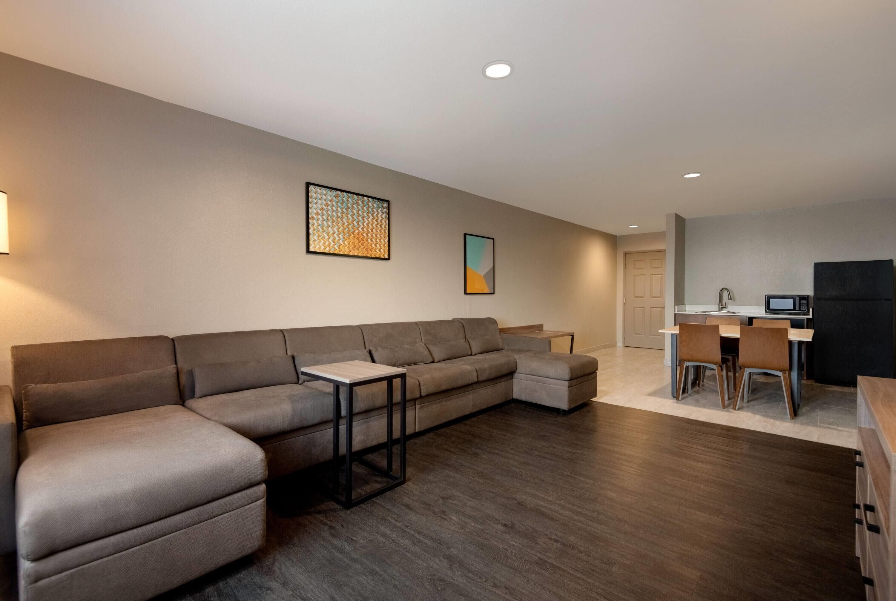 A modern living room with a sectional sofa, a small table, and a kitchen area with a dining set.