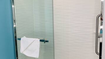 A glass-enclosed shower with a handheld showerhead, a towel rack, and a toilet visible in the adjacent room.