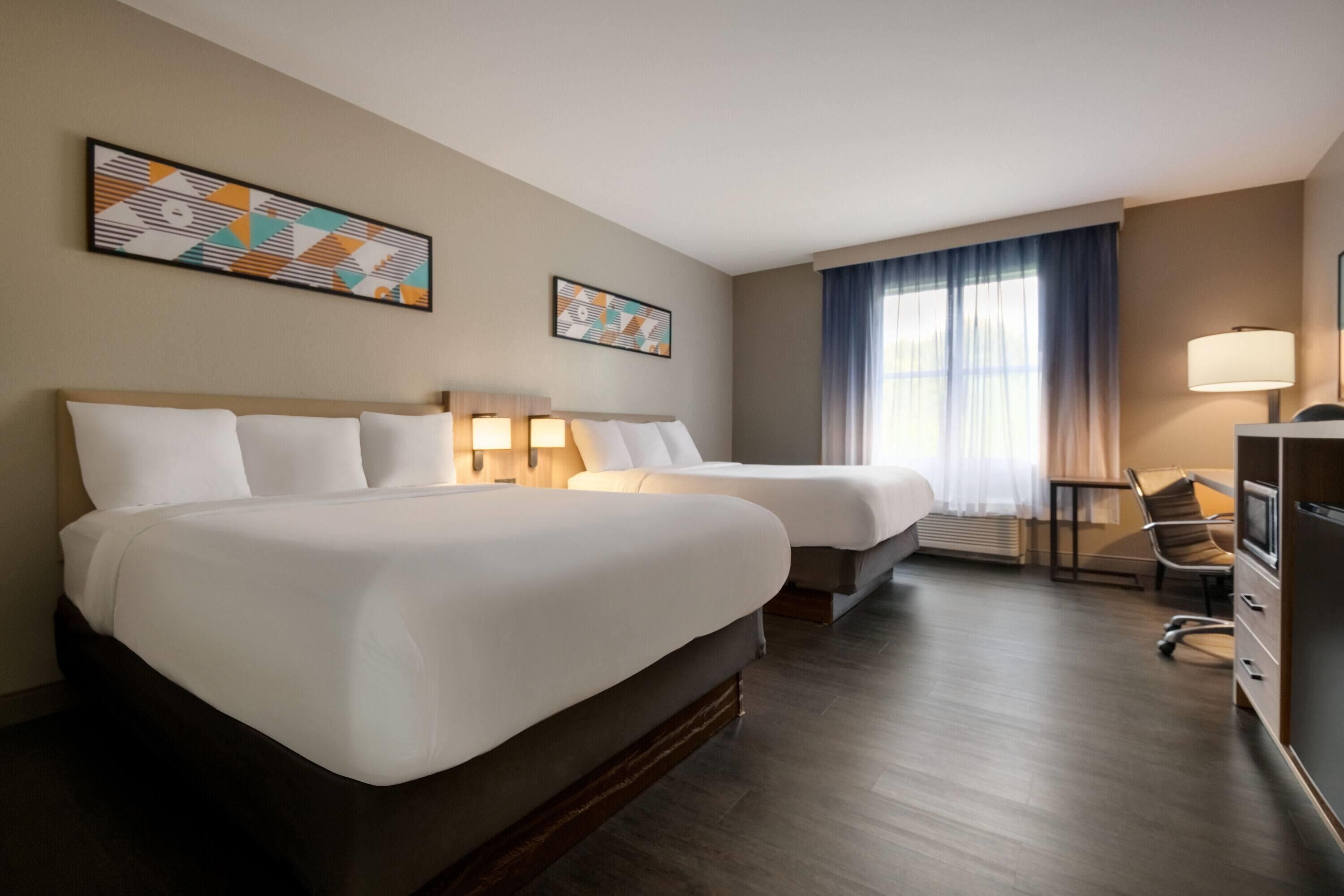 A hotel room with two beds, a desk, a chair, and a TV.