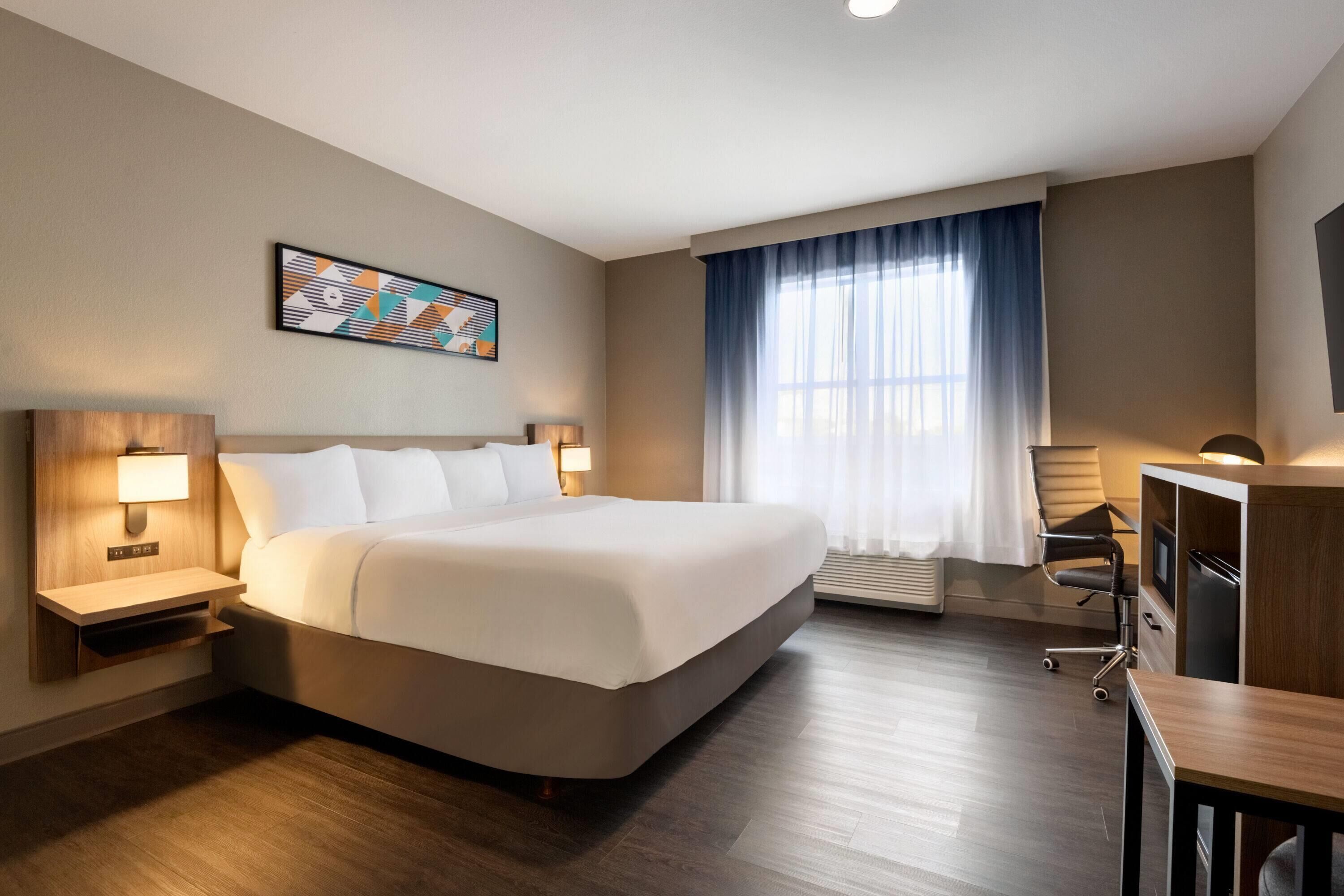 A hotel room with a large bed, a desk, a chair, a TV, and a window with curtains.