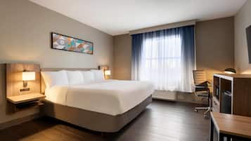 A hotel room with a large bed, a desk, a chair, a TV, and a window with curtains.