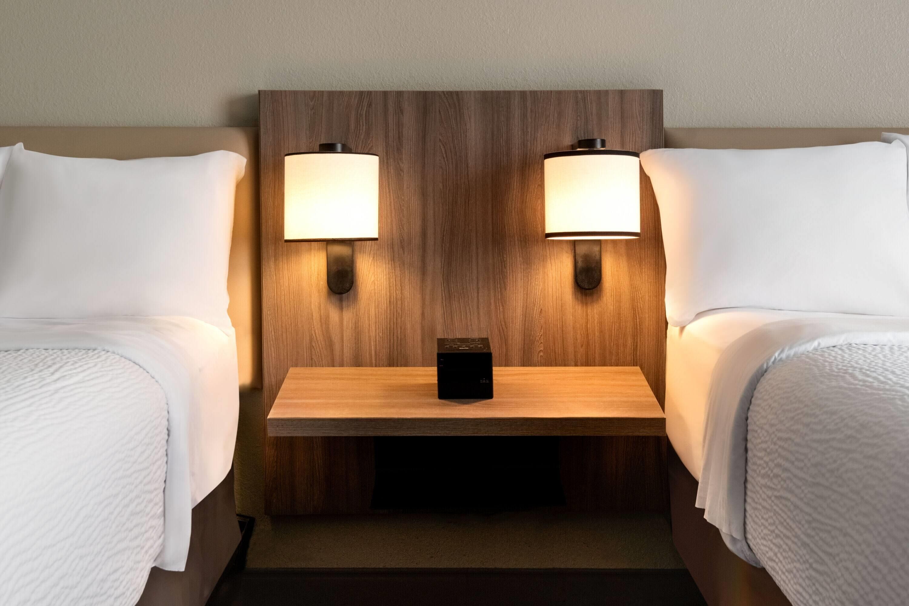 Hotellihuone, jossa on kaksi sänkyä, puinen pääty ja kaksi yöpöytävalaisinta.