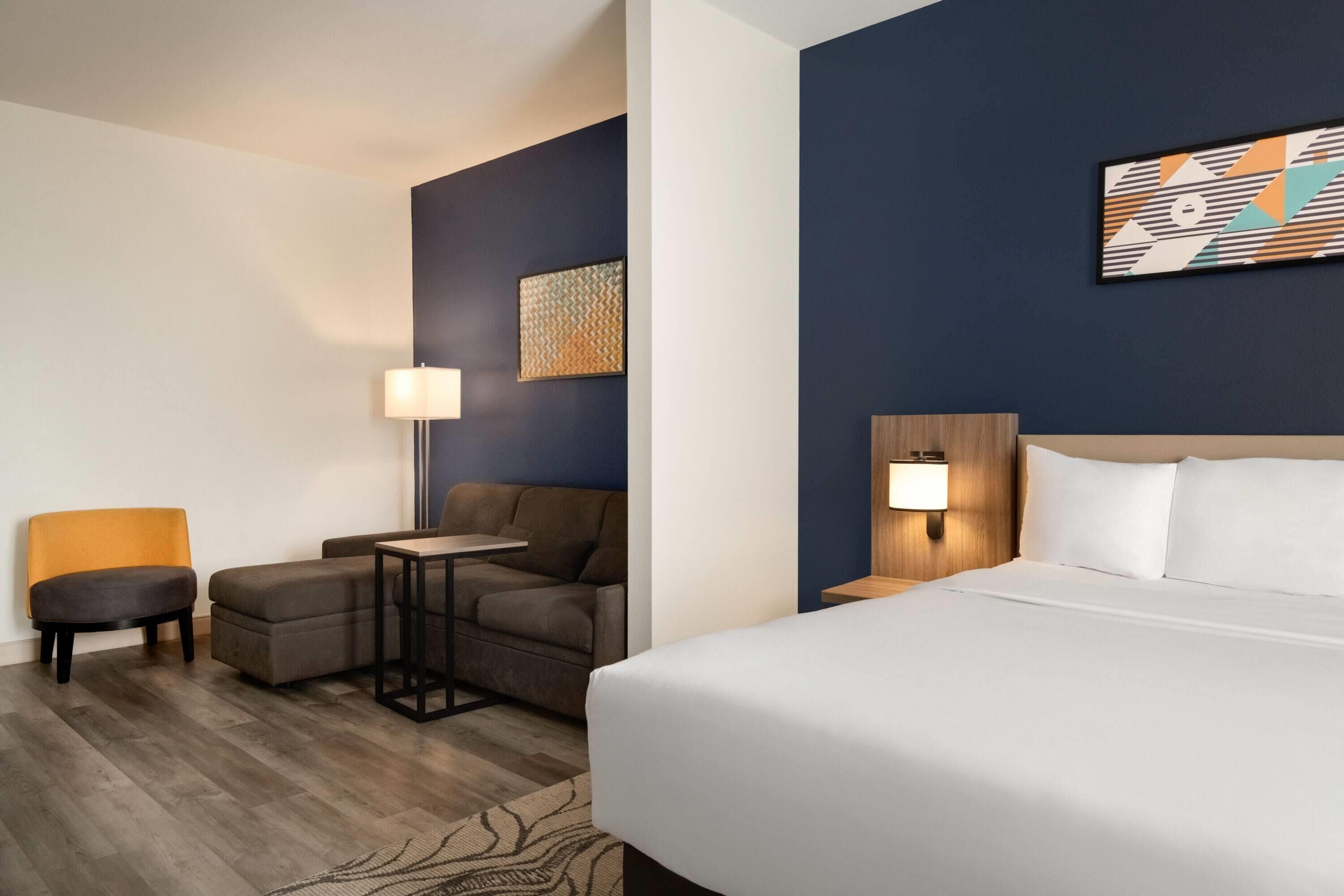 A hotel room with a bed, a sofa, a small table, and a chair.