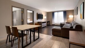 A modern hotel room with a dining area, a sofa, a TV, and a lamp.