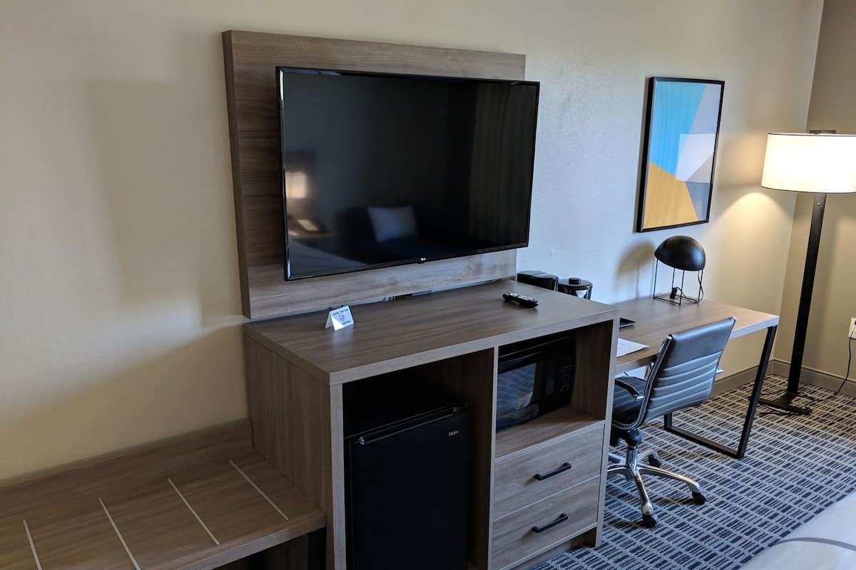 A hotel room with a TV, desk, chair, and a lamp.