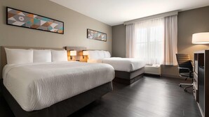 A hotel room with two beds, a desk, a chair, and a large window with curtains.