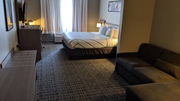 A hotel room with a bed, a desk, a chair, a sofa, and a large window with curtains.