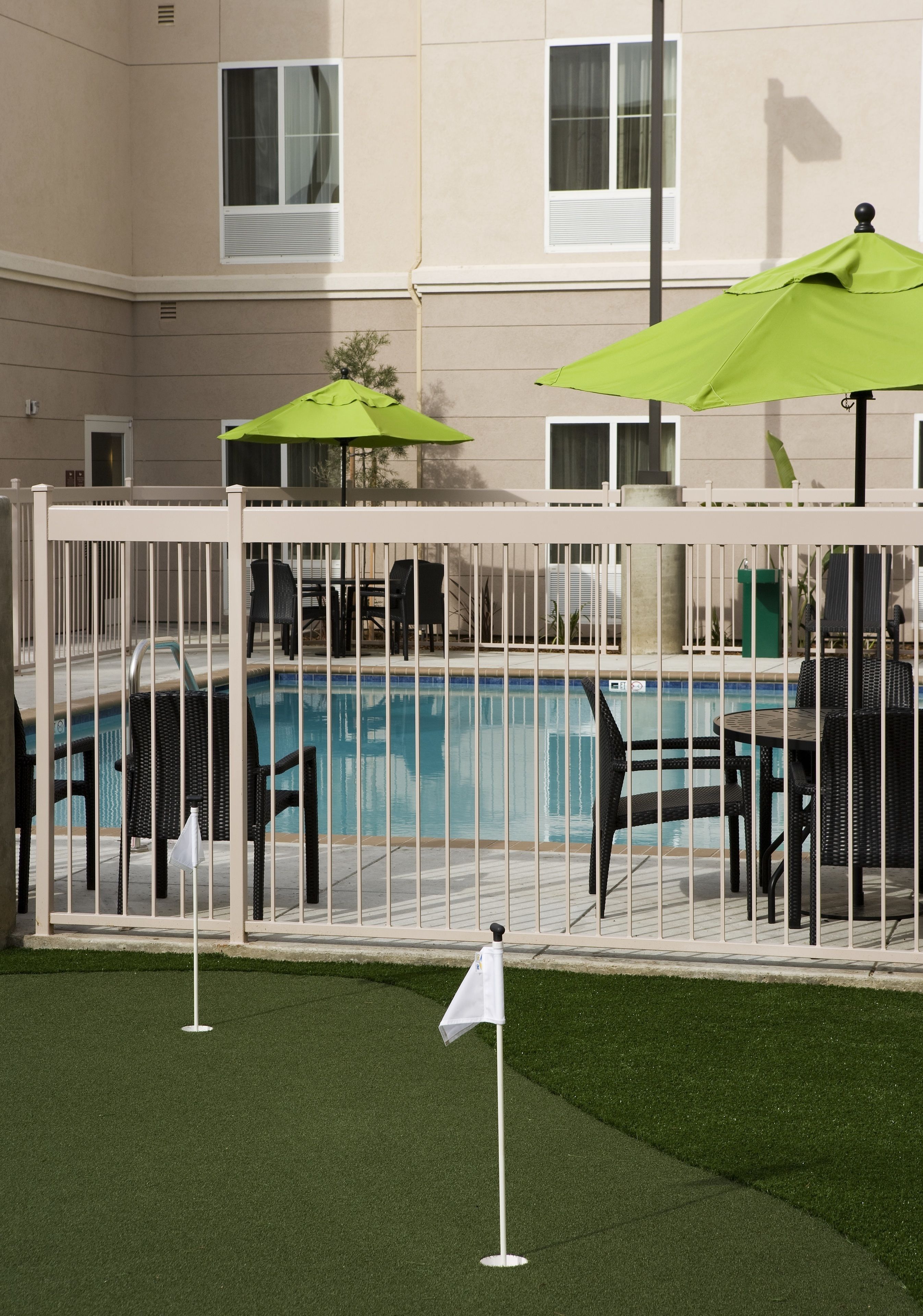 Zona de piscina con piscina cercada, sillas de descanso y una bandera en el césped.